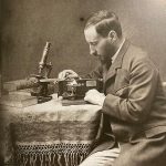 A photographical self-portrait of Cajal showing the artist with a microscope seated at a desk, from around 1890.