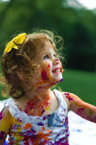 Young female child having fun, smiling and covered in paint splodges