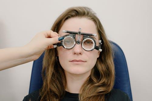 Young girl sitting in optician's seat getting her eyes tested with the optician holding the lenses in from of the test glasses