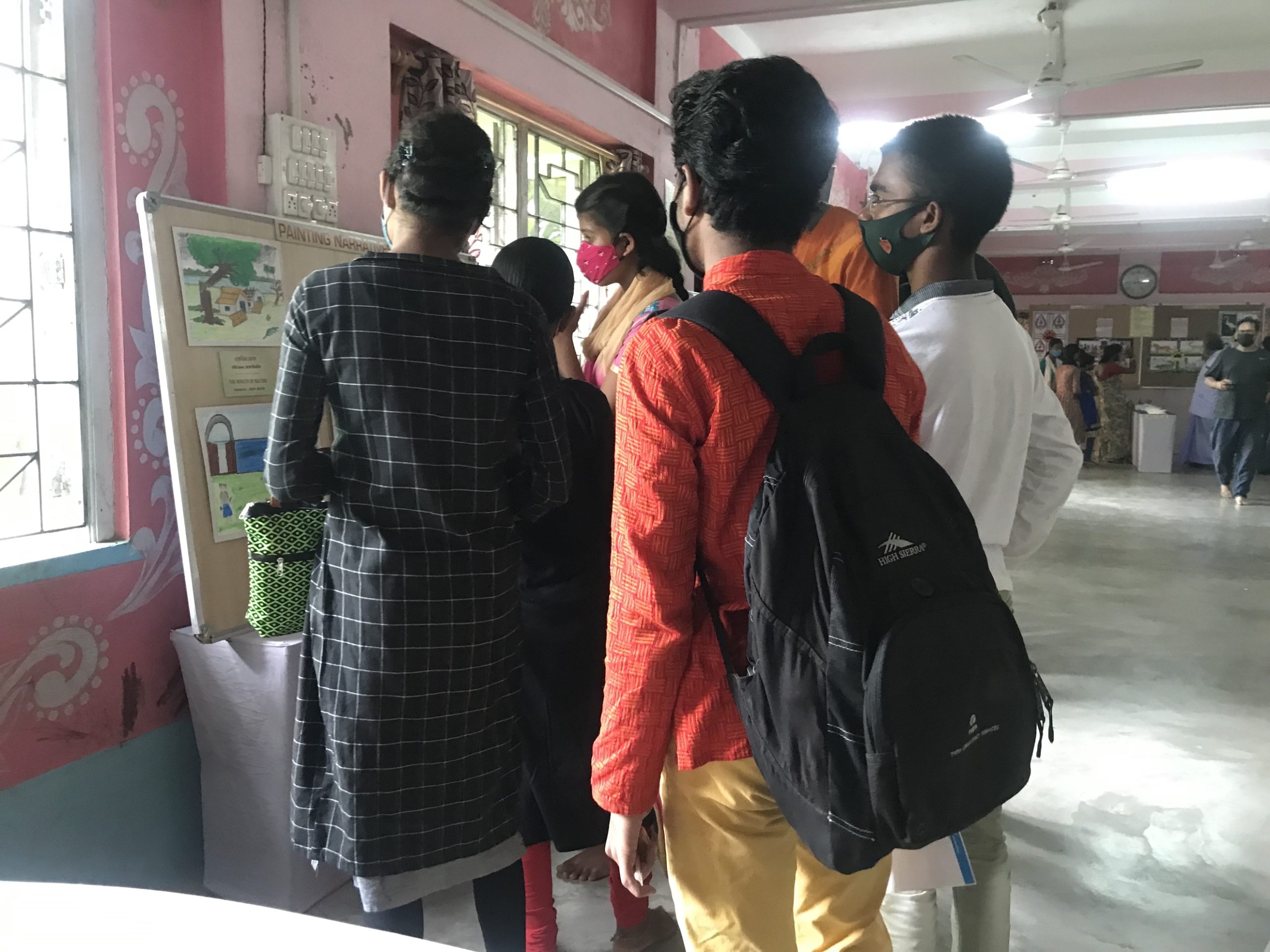 Photograph of a small group of students looking at a board with drawings on it, India