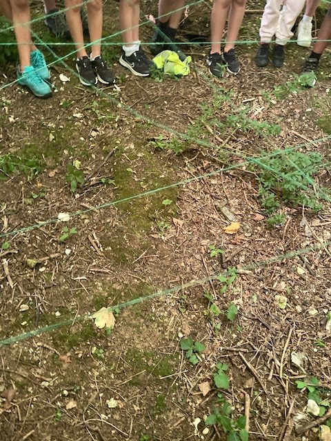Photograph of seven students' feet on a grassy area, with a green twine webbed in front of them