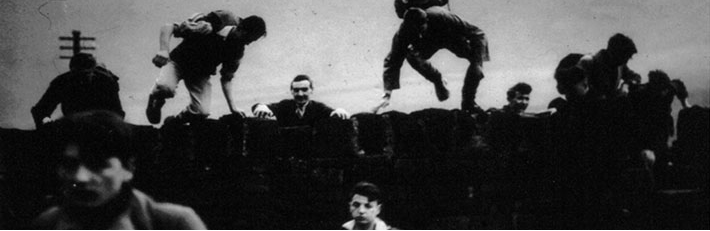 An old black and white photograph of men climbing over a stone wall on a moor