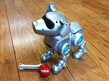 A photograph of a toy robot puppy, with a toy bone and a red ball with the brand name Tekno printed on it at its feet.