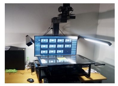 Image credit: Digitisation rig. Photograph by Karen Smith (2024). Used with kind permission. All rights reserved. Photograph of the digitisation rig used at the University of Sussex, showing an overhead camera above a horizontal glass platen and a computer screen