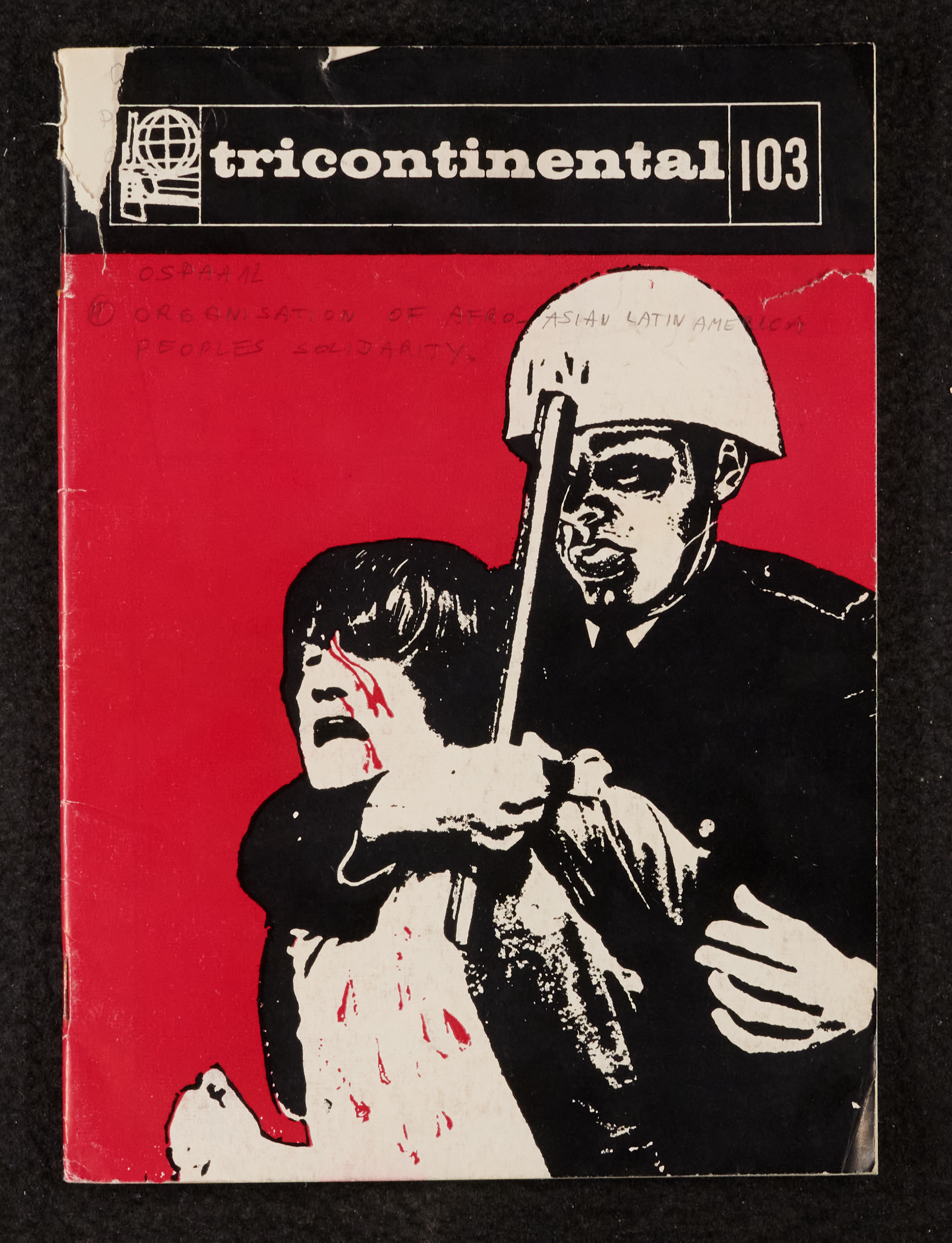 Image credit: Copyright OSPAAAL (1977). Tricontinental Review, no. 103 (1977): Front cover. Accessed via British Library for Development Studies Legacy Collection. Scan courtesy University of Sussex (2024). All rights reserved. The front cover of Tricontinental Review, no. 103 (1977), shows a black-and-white drawing of a military person in a helmet holding a civilian from behind with his arm, holding a baton, around the civilian's neck to restrain them. The civilian has red blood spatters emanating from their head and nose, dripping across their chest. The background to the cover is red.