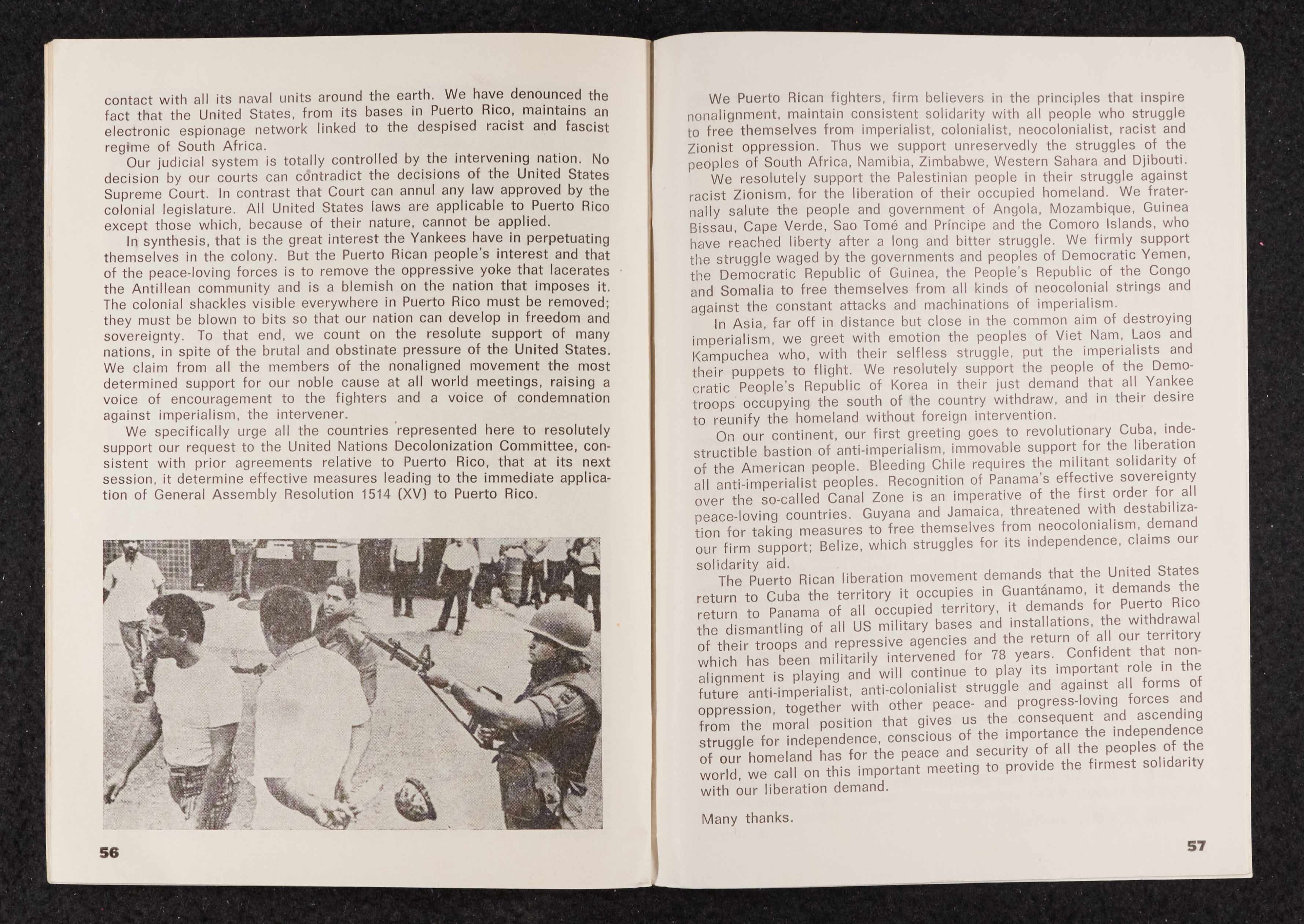 Image credit: Copyright OSPAAAL (1977). Tricontinental Review, no. 103 (1977), pp. 56-57. Accessed via British Library for Development Studies Legacy Collection. Scan courtesy University of Sussex (2024). All rights reserved. A booklet open on a double-page spread. The left-hand side is two-thirds text. There is a black and white photo at the bottom showing a soldier pointing his rifle at the heads of a group of men in civilian clothes. The right-hand side is a full page of text.