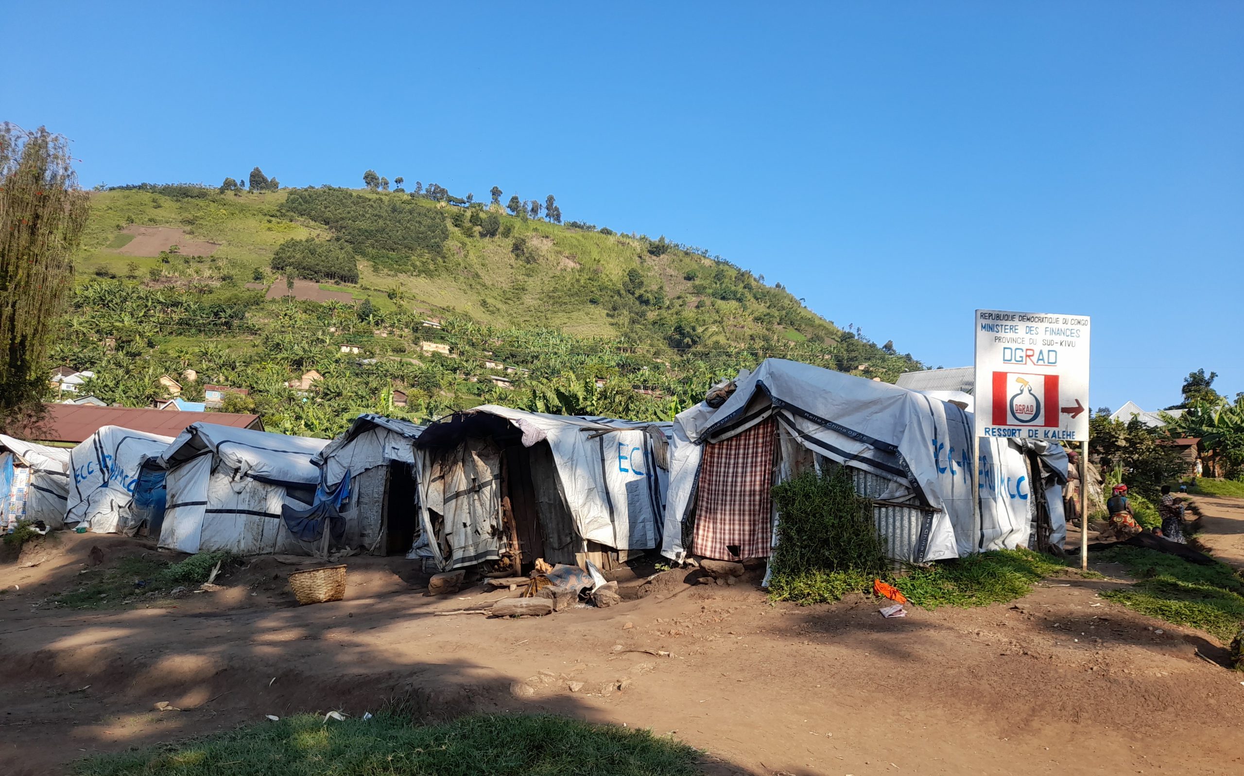 Photo of Kalehe refugee camp in the DRC. In the foreground are tents and in the background a hill covered in green vegetation rises above the camp.