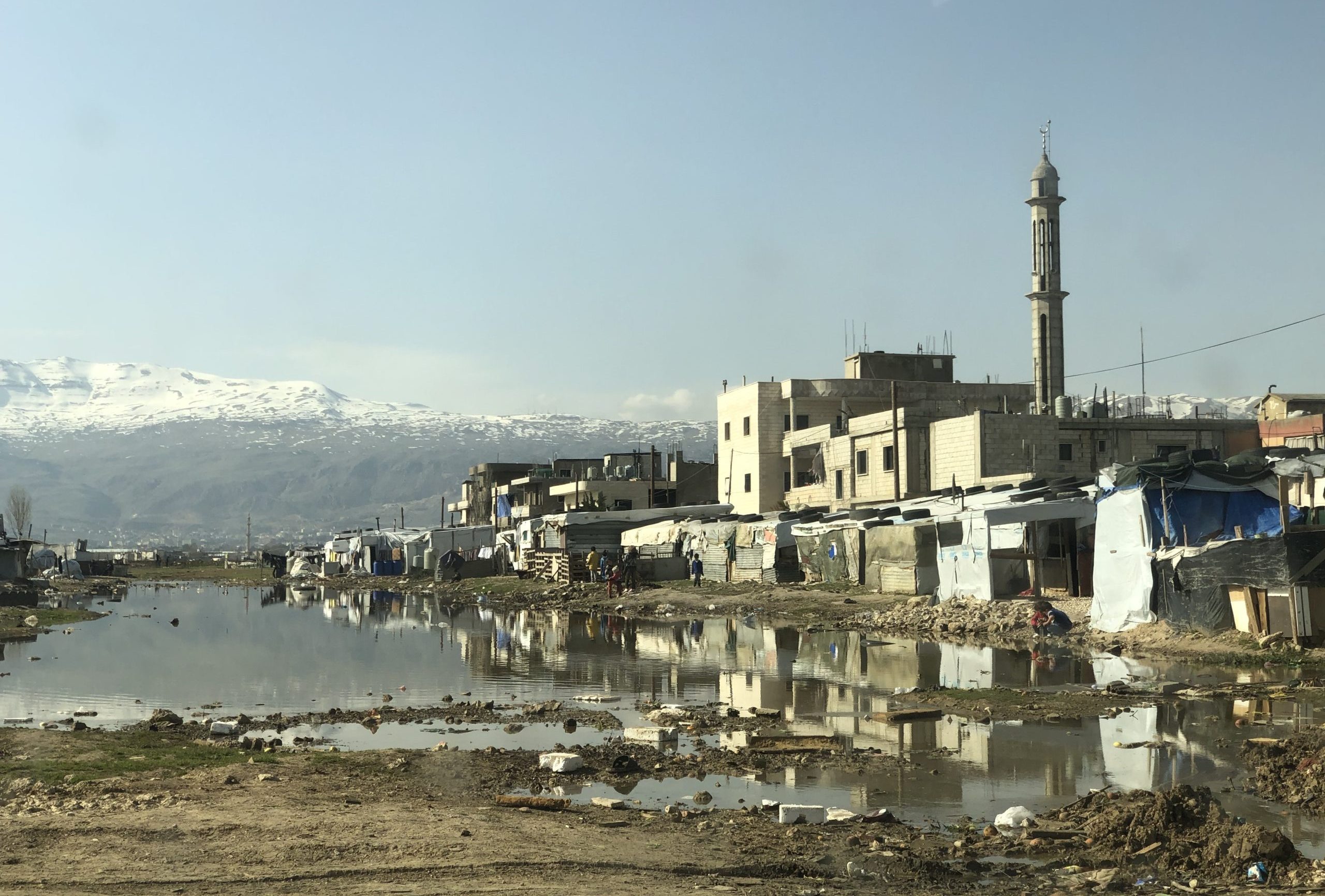 A photo of Beqaa Valley showing building reflected in the water and snow-capped mountains in the distance