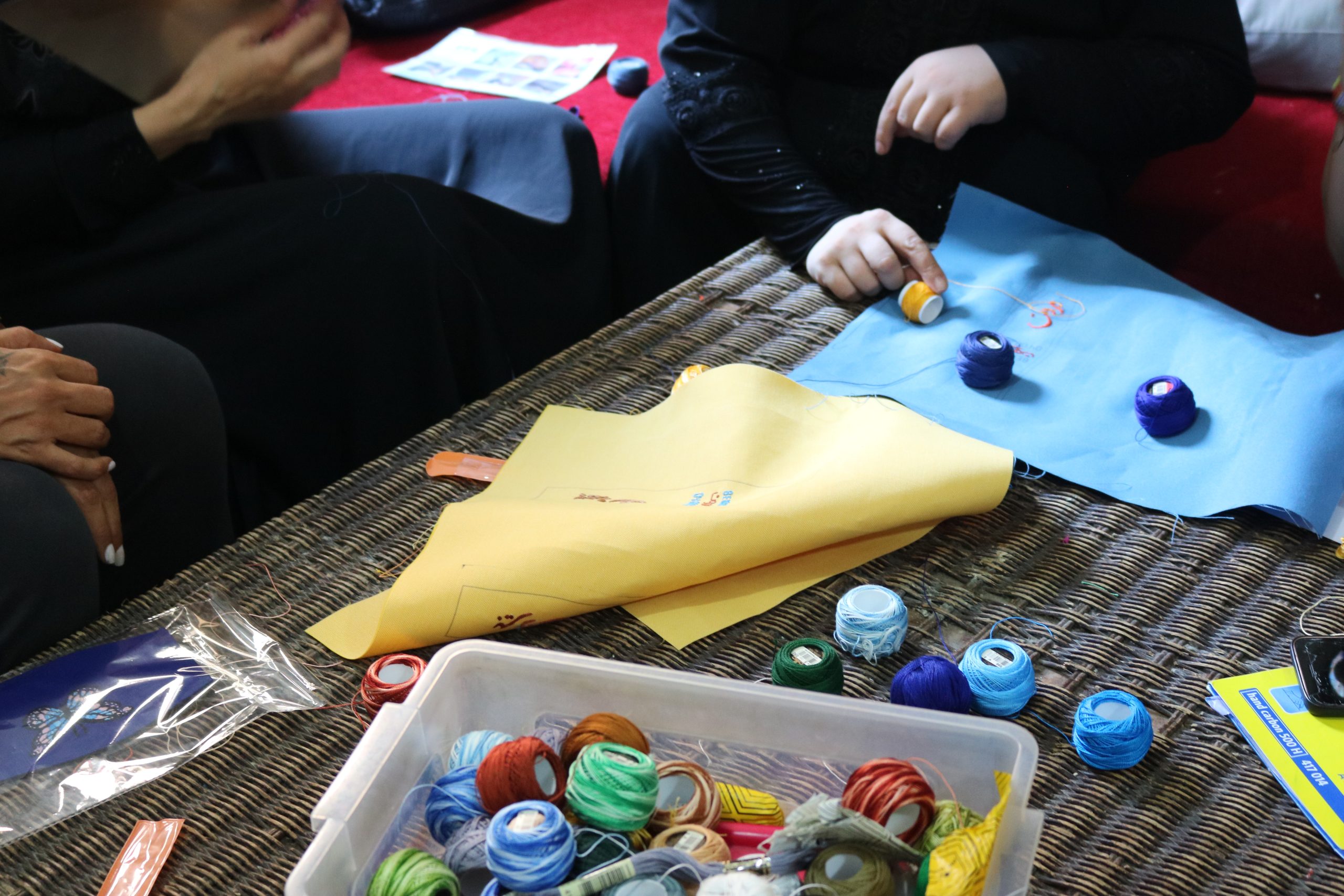 A photo of sewing materials – textiles and thread of different colours. Next to the materials women's hands are visible.