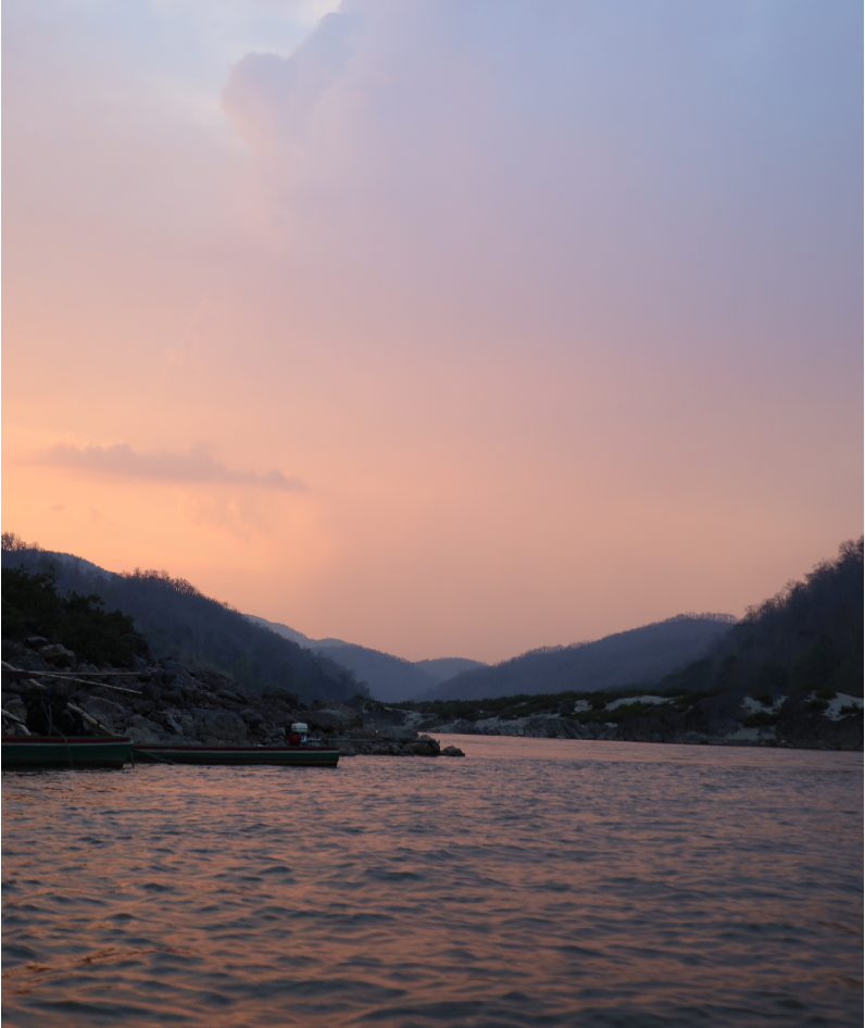 Photo of a sunset over a river, with wooded hills in the distance.