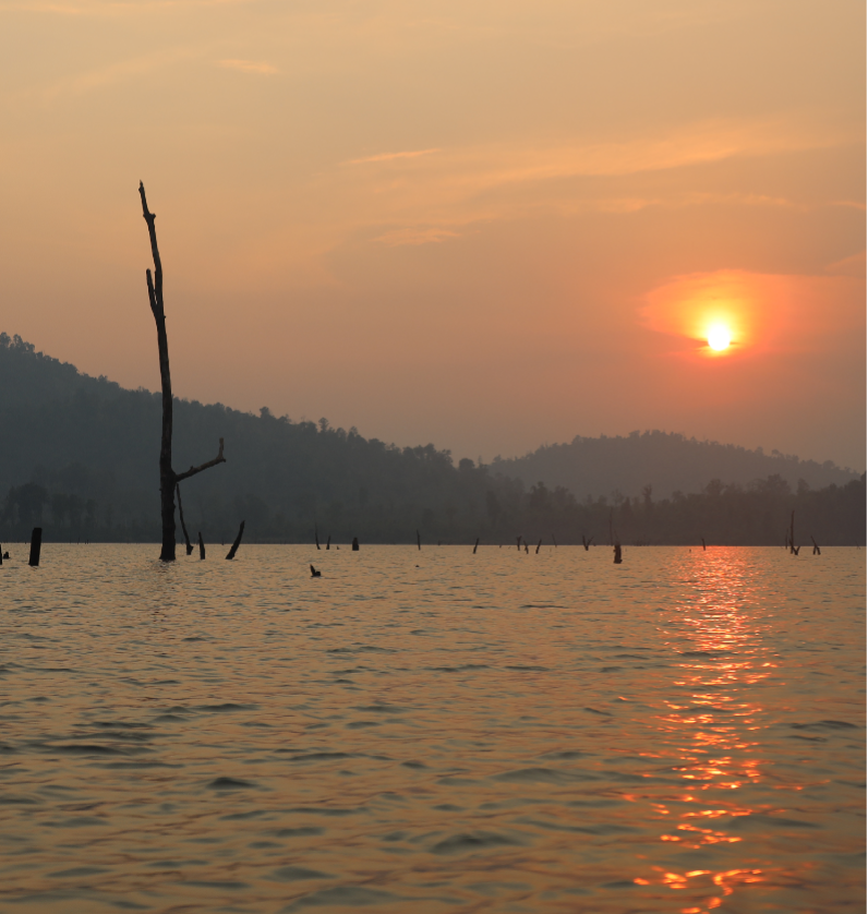 Photo of a sunset reflected in water with wooded hills in the distance.