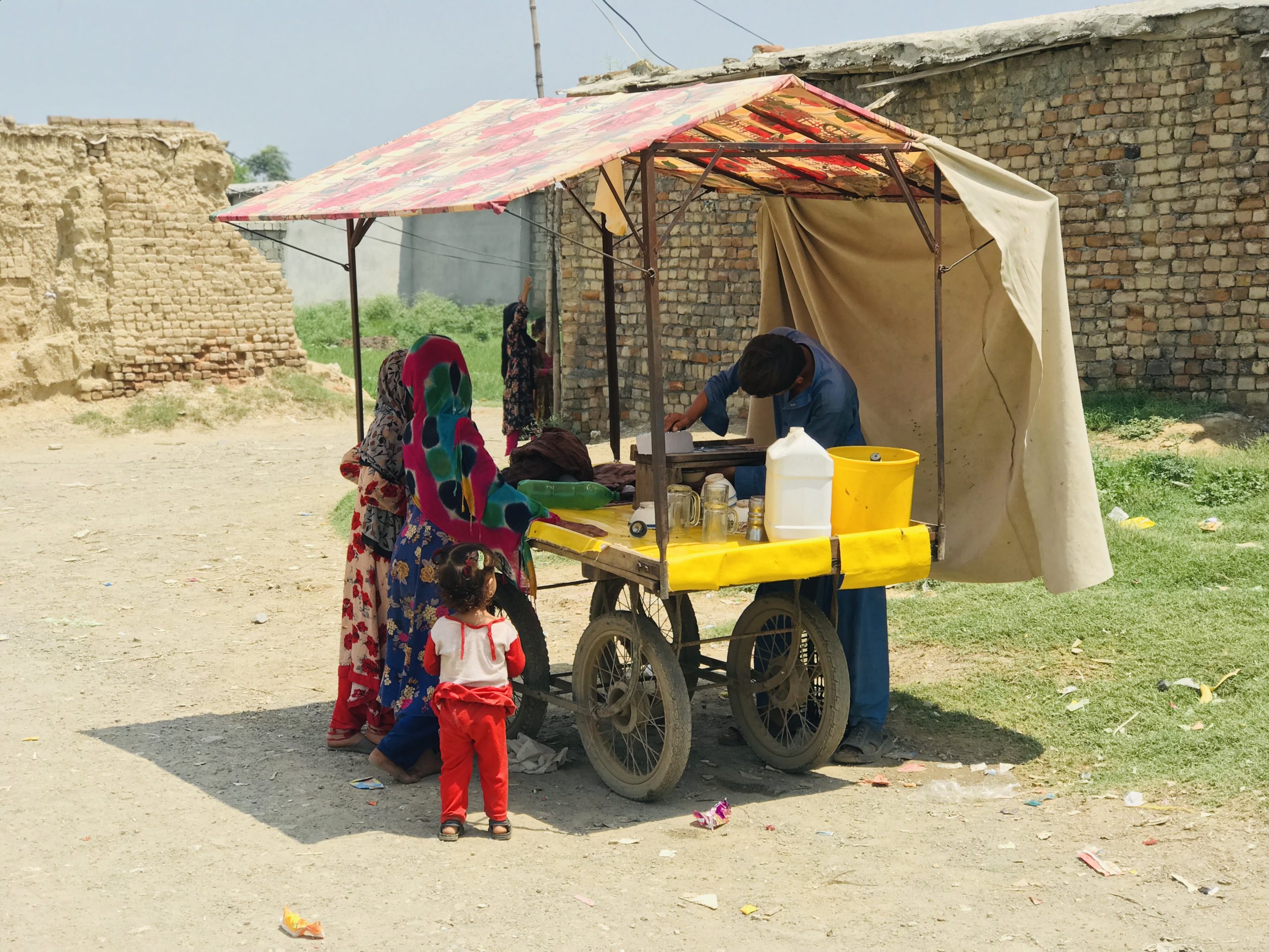 A photo of a stall selling iced treats. There are children in colourful clothing gathered around the stall.