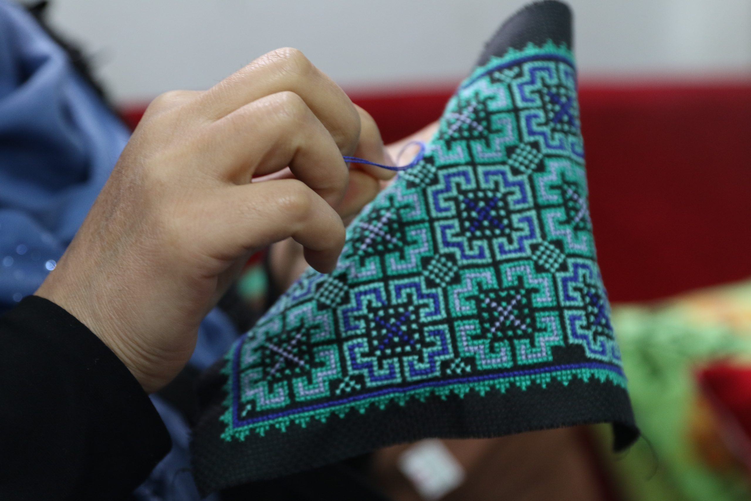 A close-up photo of a woman's hands holding a piece of embroidery and some thread.